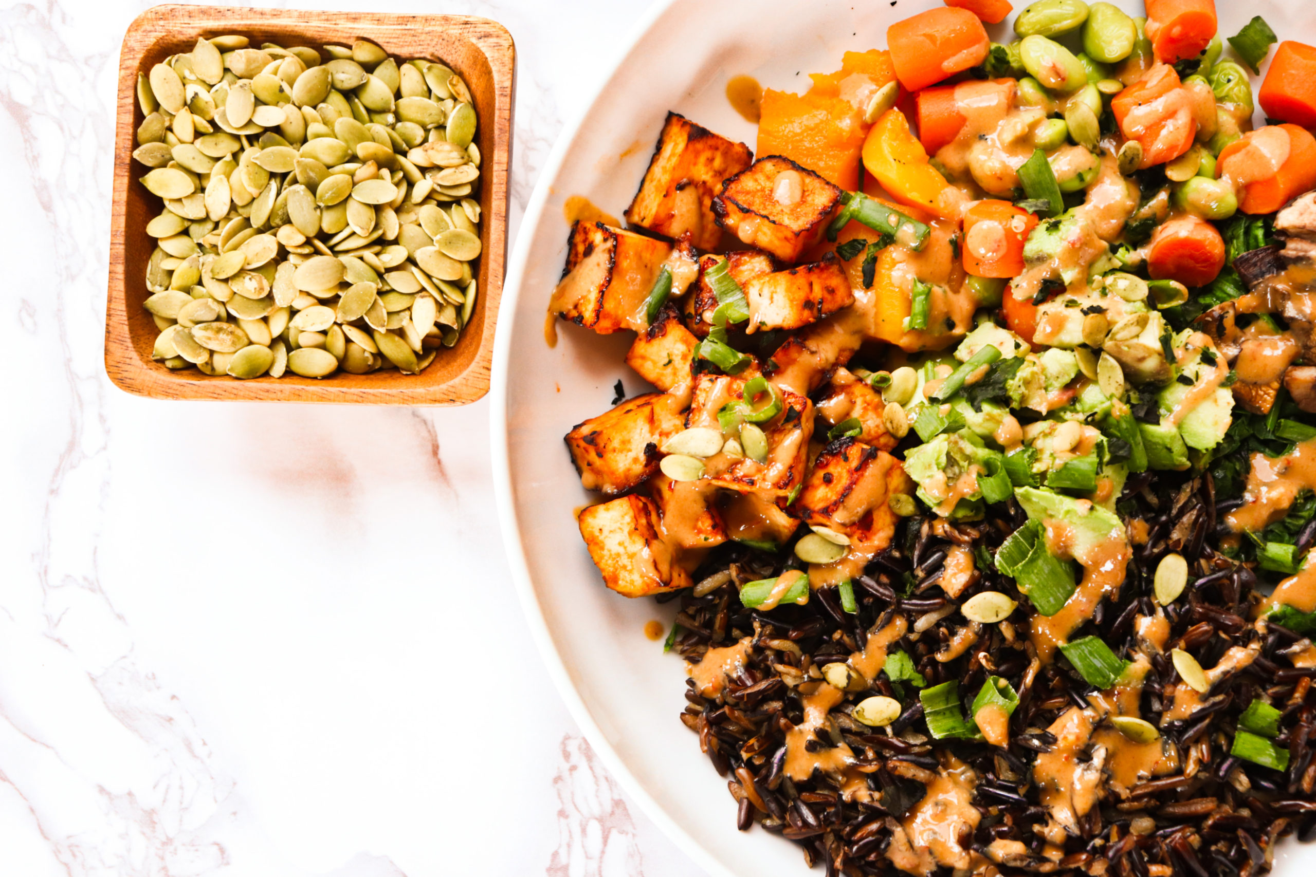 A hearty, protein filled bowl of goodness! This High Protein Mushroom Tofu Bowl is filled with wild rice, mushrooms, tofu, edamame beans, and topped with pumpkin seeds and a miso ginger dressing.